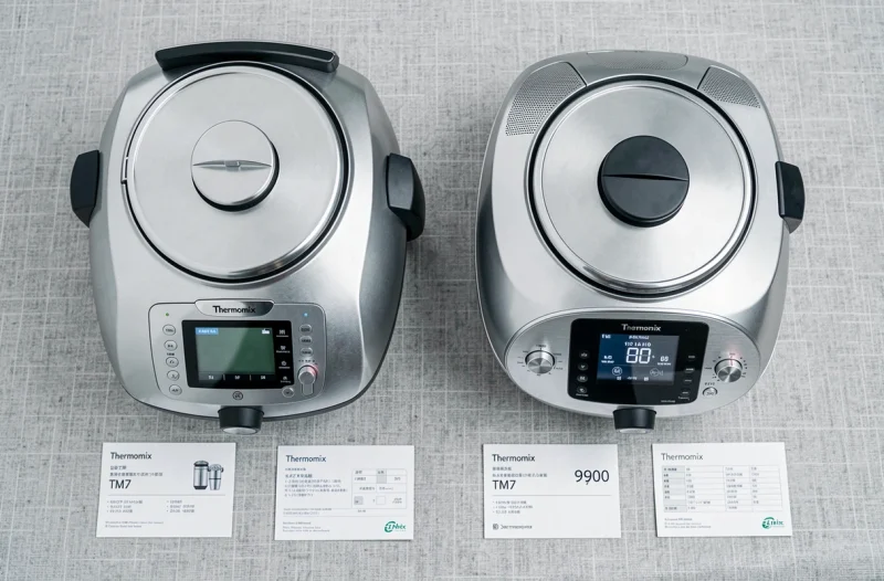 Comparaison Thermomix TM6 et TM7 en vue à plat sur fond de lin gris avec fiches techniques et étiquettes de prix
